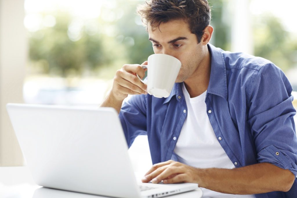 Young man drinking coffee while using at laptop
