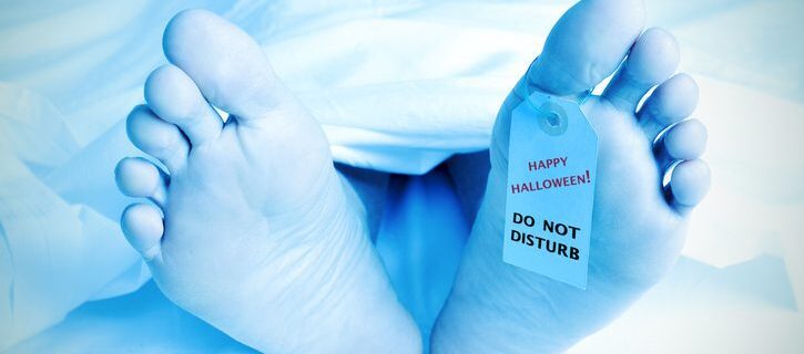closeup of the feet of a dead body covered with a sheet and with a tag tied on his big toe with the text happy halloween, do not disturb