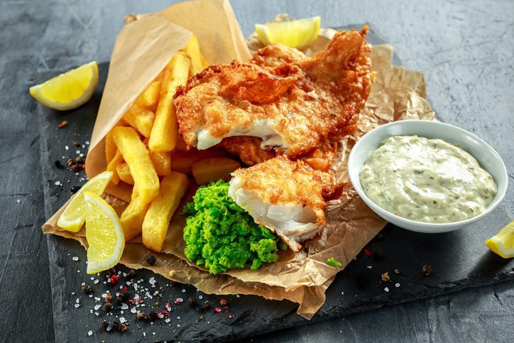 British Traditional Fish and chips with mashed peas, tartar sauce on crumpled paper