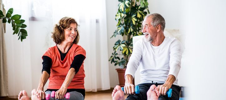 A happy senior couple with dumbbells doing exercise at home.