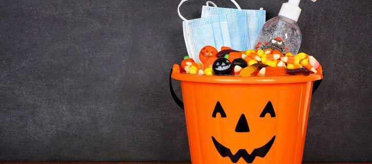 Halloween Jack o Lantern pail with candy and coronavirus prevention supplies on a shelf against a dark background