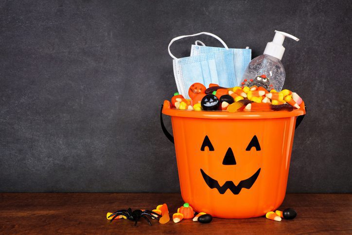 Halloween Jack o Lantern pail with candy and coronavirus prevention supplies on a shelf against a dark background