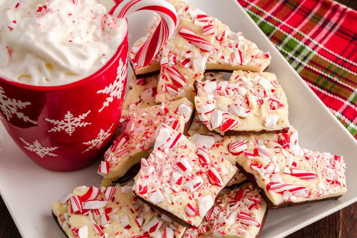 Chocolate peppermint bark on white plate with red snowflake mug filled with hot cocoa and whipped cream