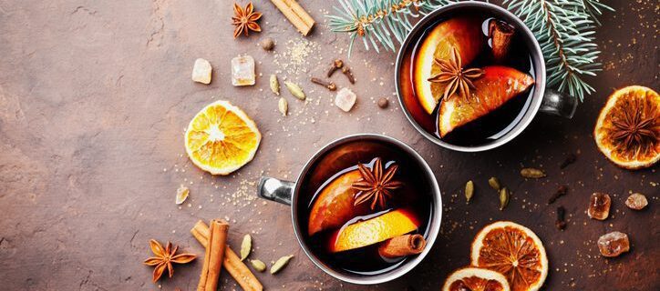 Two cups of christmas mulled wine or gluhwein with spices and orange slices on rustic table top view. Traditional drink on winter holiday. Flat lay.