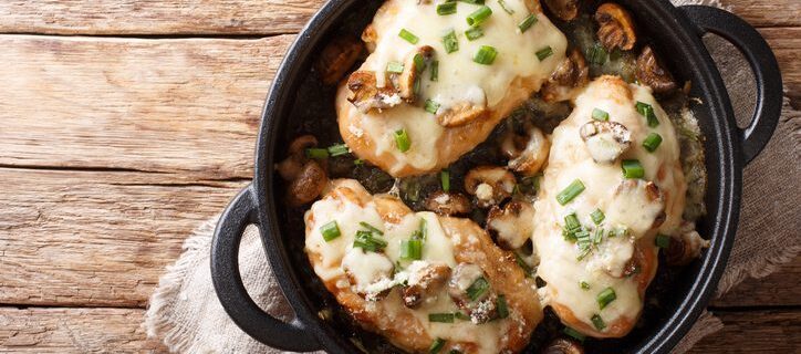 Lombardy Chicken breasts cooked with mushrooms, green onions, mozzarella cheese and parmesan closeup in a pan on the table. Horizontal top view from above