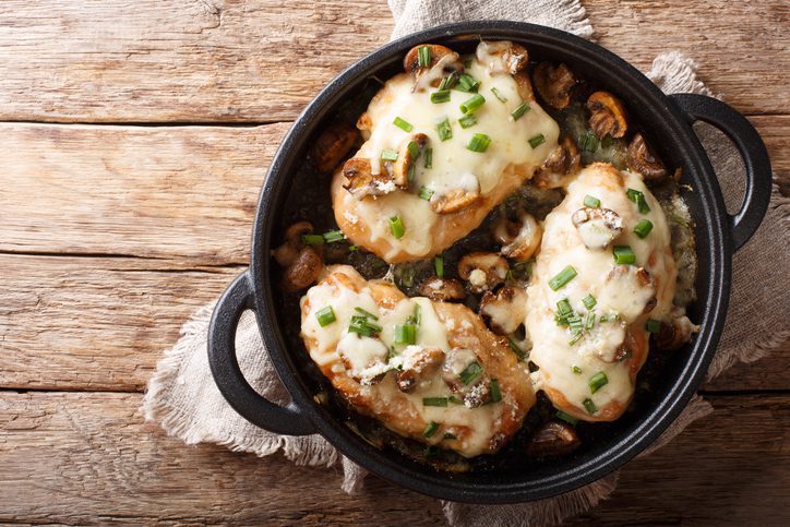 Lombardy Chicken breasts cooked with mushrooms, green onions, mozzarella cheese and parmesan closeup in a pan on the table. Horizontal top view from above