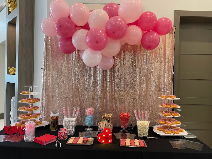 table with assorted candies in front of a pink sparkle background with pink balloons