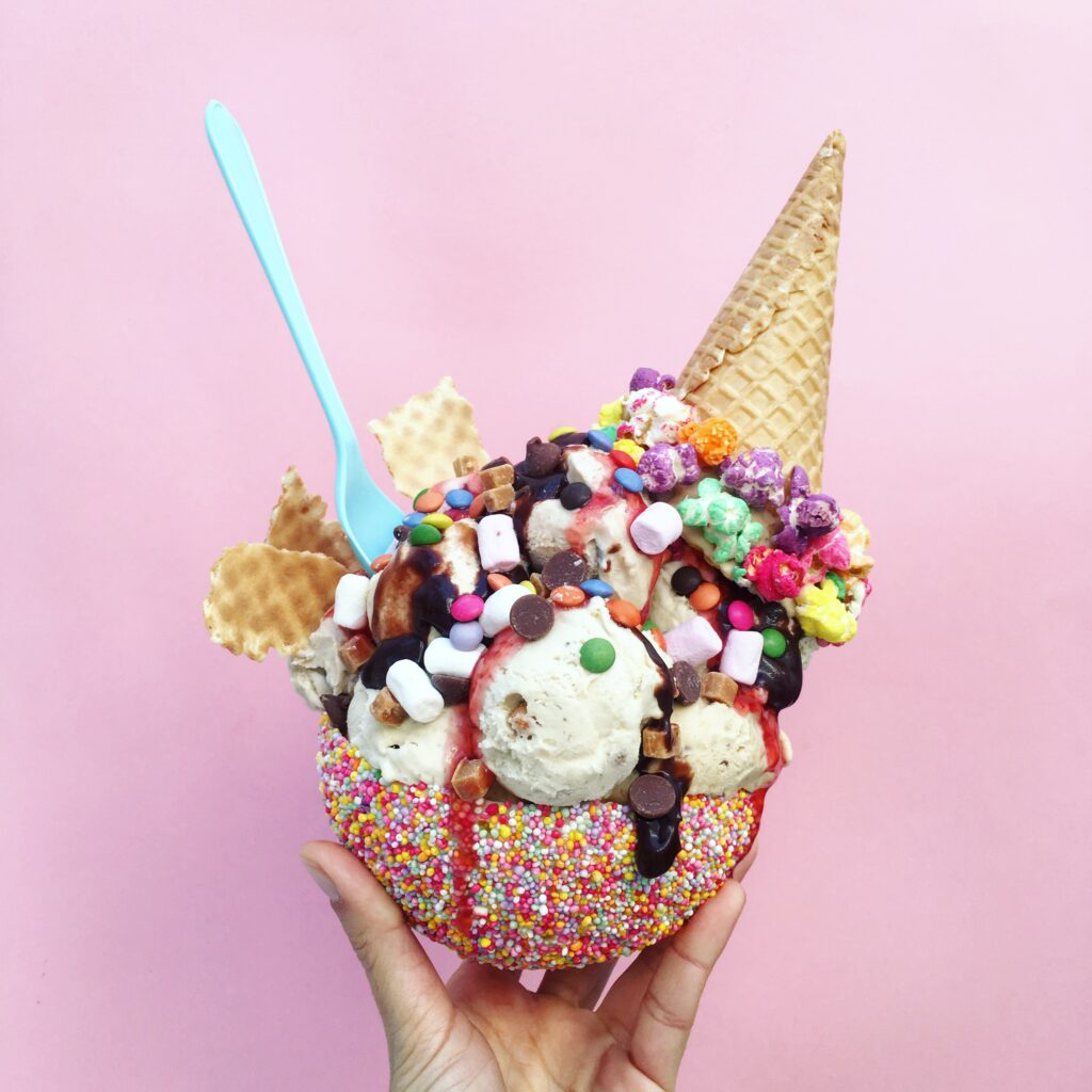 hand holding an ice cream sundae with lots of sprinkles, candy, and waffle cone toppings