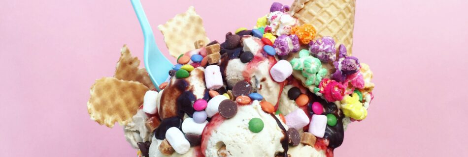 hand holding an ice cream sundae with lots of sprinkles, candy, and waffle cone toppings