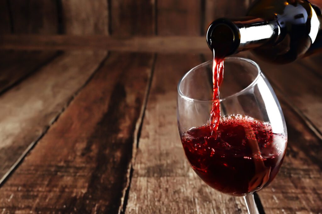 Red wine is poured from bottle to glass, wooden background