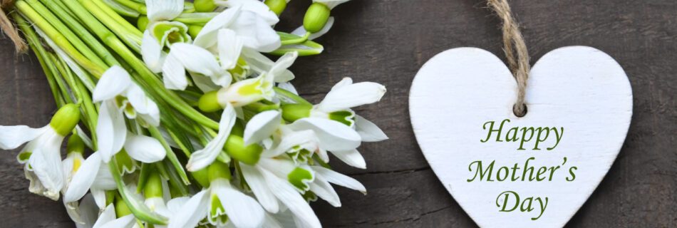 Happy Mother's Day greeting card with snowdrop spring flowers and decorative heart with text on old wooden table. Springtime holidays background. Selective focus.